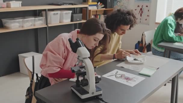 Wysoki Kąt Kaukaskiej Dziewczyny Patrzącej Mikroskop Piszącej Notatniku Siedzącej Biurkiem — Wideo stockowe