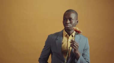 Gri ceketli, sarı gömlekli, elinde çiçekle kameraya poz veren yakışıklı, genç ve yetişkin bir adamın yatay yavaş çekimi.