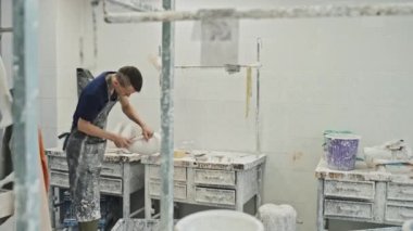 Özürlü genç bir adam atölyesinde protez bacak için soket işçiliği yapıyor. El aletleriyle alçı şekillendiriyor.