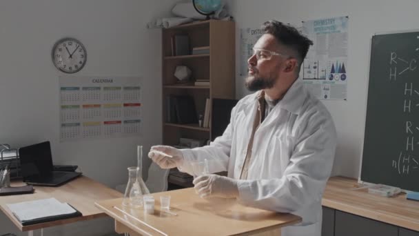 身穿医用长袍 戴防护护目镜的中长男教师站在黑板前 进行化学实验课 — 图库视频影像