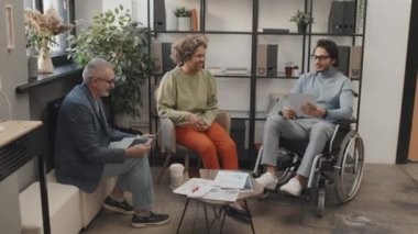 Siyah kız, Kafkasyalı kıdemli bir adam ve tekerlekli sandalyedeki Orta Doğulu meslektaşın evraklarla çalışırken, öğleden sonra ofiste konuşurken.