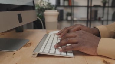 Gündüz vakti masa başında bilgisayarın klavyesine yazı yazan kırpılmış bir adamın elleri.