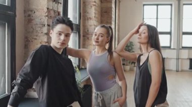 Gündüz vakti modern dans stüdyosunda dikilip kameraya bakan iki genç kızın orta boy portresi.