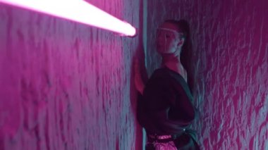 Orta boylu, güzel elbiseli bir kız. Duvarda pembe neon ışıkta hareket ediyor ve poz veriyor.