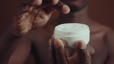 Seçici odak noktası, tanınmayan Afrikalı Amerikalı adamın az miktarda besleyici krem alıp vücuduna sürmesi.