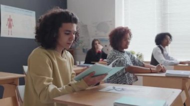 Orta boylu, koyu saçlı, genç bir çocuk sabahları sınıfta oturuyor.