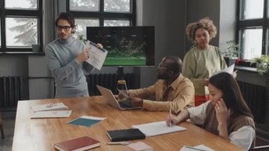 Orta uzunluktaki balıkçı yakalı zeki Orta Doğulu adam öğleden sonra konferans odasında çok ırklı meslektaşlarına sunum yapıyor.