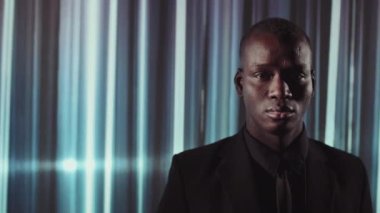 Siyah takım elbiseli yakışıklı Afrikalı bir adamın fütüristik çizgili neon arka planda kameraya baktığı yatay yakın plan.