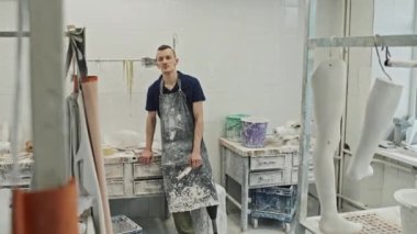 Protez üretim fabrikasında önlük takan engelli genç beyaz bir adamın orta boy portresi. Kameraya bakıyor.