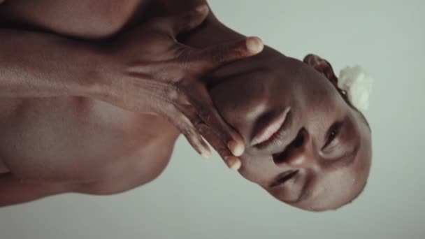年轻的性感黑人男子的垂直画室肖像 他的耳朵后面挂着玫瑰花 镜头慢慢地抚摸着他的脖子和下巴 — 图库视频影像