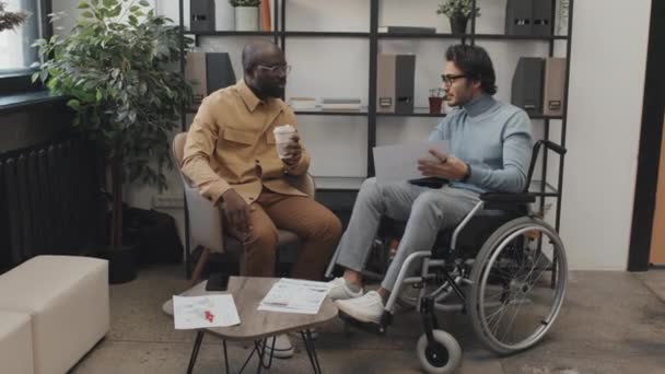 昼間に車椅子で中東の男性同僚と話すシャツを着たアフリカ系アメリカ人男性の完全なショット — ストック動画