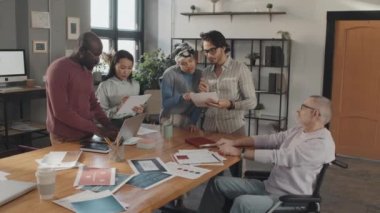 Gündüz vakti konferans masasında durmuş, konuşan, tekerlekli sandalyedeki kıdemli genç iş arkadaşlarının orta yavaş çekimleri.