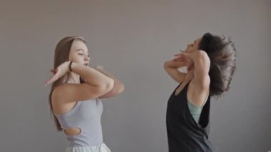 Gün ışığında açık gri duvarın önünde Vogue hareketleri gösteren iki güzel kızın orta açılı portresi.