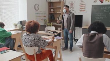 Kafkasyalı erkek profesörün yüz maskesi taktığı ve sabahları masalarında oturan genç öğrencilere anatomi dersi verdiği geniş açı.