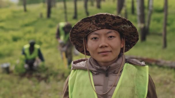 夏の日に緑の森の中に立つ帽子の若いアジアの女性の森の肩の上の肖像画 カメラを見て — ストック動画