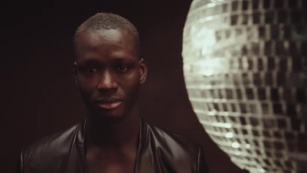Stilvoller Afroamerikanischer Mann Lederjacke Steht Studio Mit Dunkelbraunem Wandhintergrund Beleuchtet — Stockvideo