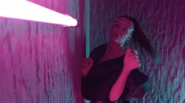 Göze çarpan kıyafetli, pembe neon ışıkta duvardan duvara poz veren güzel bir kızın görüntüsünü izliyoruz.