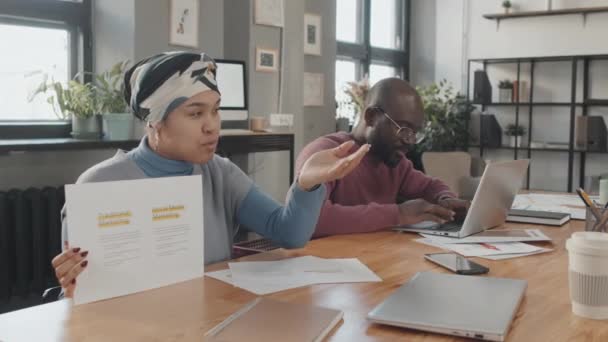 上午在会议室举行的情况介绍会上 年轻黑人男子在手提电脑上打字 非洲裔美国女孩把文件拿给看不见的同事看 — 图库视频影像
