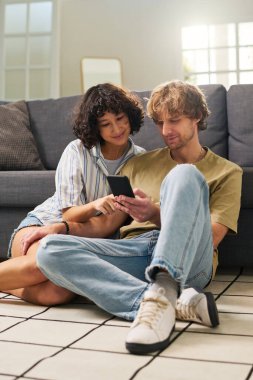 Genç adam ve karısı online menü puanlarını karıştırıyor ve kanepede dinlenirken yemek seçiyorlar.