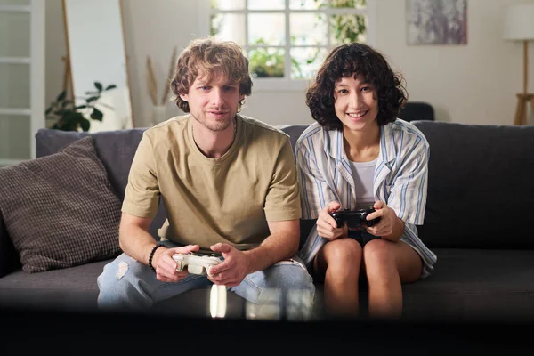 幸せな若いです女性と彼女の夫とともにジョイスティック遊びビデオゲームながら座っています上のカウチでテレビの前にリビングルームに設定されているレジャー — ストック写真