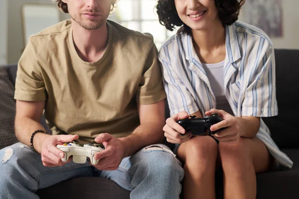 テレビのセットの前にソファに座っている間にゲームパッド上の若いカップルのプレスボタンのクローズアップと一緒にビデオゲームをプレイ — ストック写真