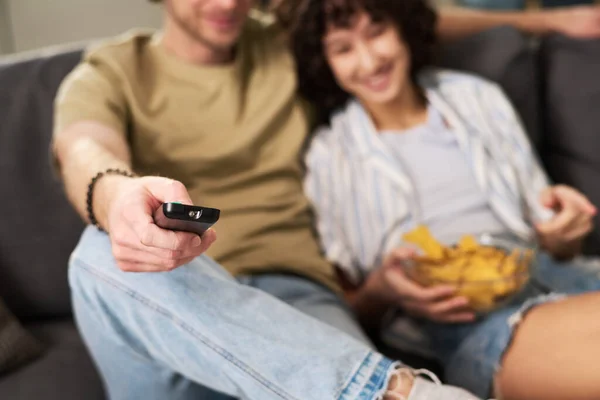 把注意力集中在手握遥控装置 拿着薯片坐在妻子身边 选择电视频道的年轻而安详的男人身上 — 图库照片