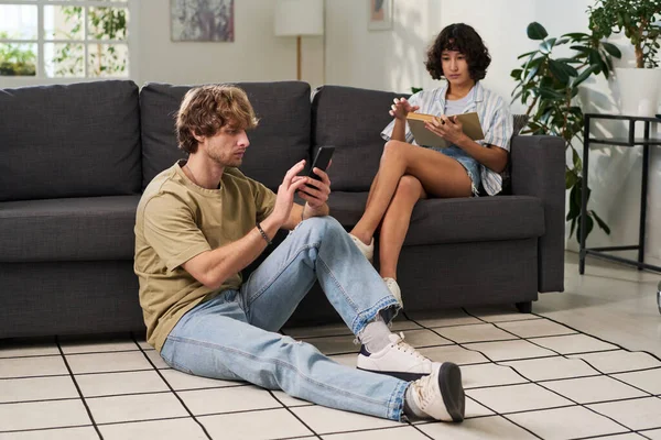 Młody Człowiek Telefonem Komórkowym Siedzący Podłodze Piszący Sms Przeciwko Żonie — Zdjęcie stockowe