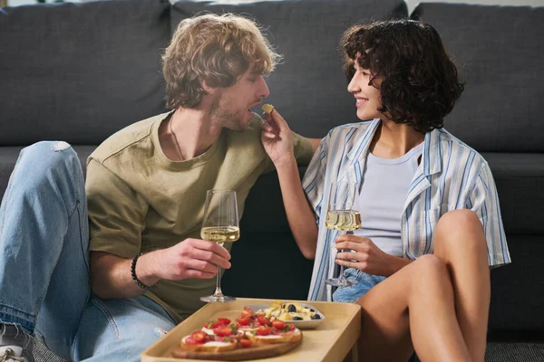 幸せな若いです女性でフルートのシャンパンまたはいくつかの他の白ワイン彼女の夫を見て 彼にチーズの小片を与える — ストック写真