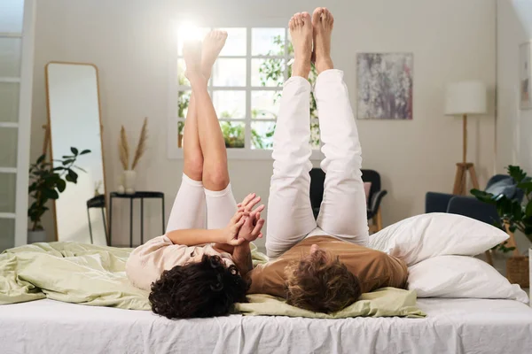 年轻而安静的赤脚异性恋夫妇 穿着白色裤子 双腿高高地躺在双人床上 手牵手 — 图库照片
