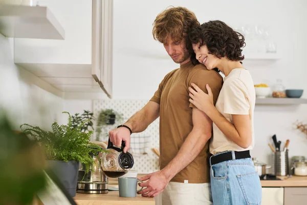 面带微笑的女人站在丈夫身边 用灰色的杯子倒着咖啡 抱着他 期待着吃早饭 — 图库照片