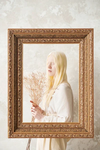 年轻和平的白化病妇女 紧闭双眼 手持枯萎的花朵 站在相框后面靠着白墙 — 图库照片