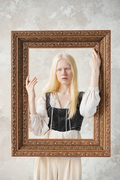 穿着中世纪服装的可爱的白化病姑娘站在大画框后面 手牵着大画框 在摄影棚拍照时摆姿势 — 图库照片