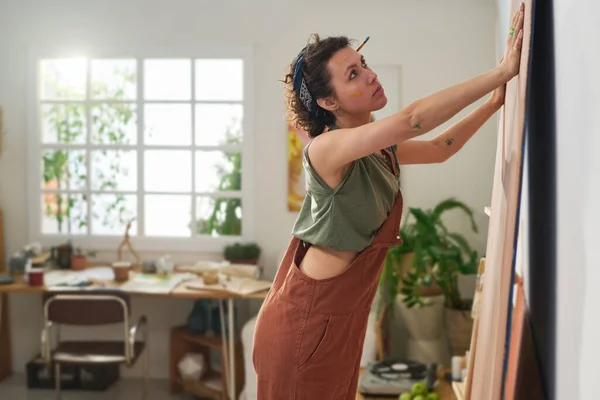 ホームスタジオの壁の前に立ち 新しい作品を作るためのパネルを準備カジュアルな服装で若い創造的な女性画家 — ストック写真