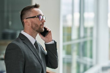 Şirketin kendine güvenen genç yöneticisinin, çalışanlarından biriyle kameranın önünde akıllı telefondan konuşmasının yan görüntüsü.