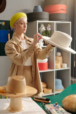 Akıllı günlük giysiler içindeki genç bir zanaatkar müşterilerinden biri için yeni keçeli şapka yapıyor.