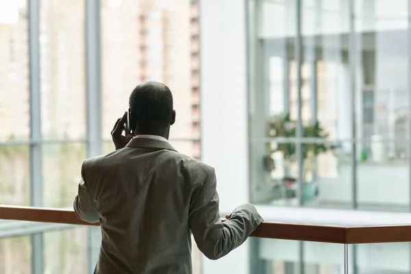非洲裔美国男性首席执行官站在办公室中央栏杆边一边用手机交谈的背景图 — 图库照片
