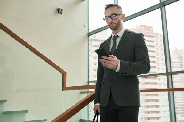 年轻的首席执行官办公室 身穿雅致的西服 戴着眼镜 站在商务中心楼梯之间 用手机办公 — 图库照片