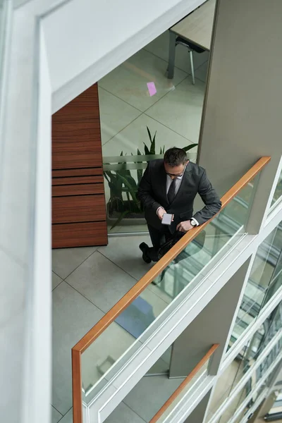 上图是一位穿着得体的年轻商人站在现代办公中心透明的栅栏边 一边用智能手机发短信 — 图库照片