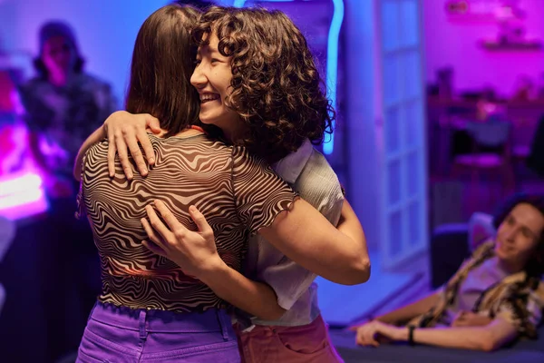パーティーで挨拶しながら抱き合っている二人の幸せな異文化間の女の子彼らの友人のアパートで行われる — ストック写真