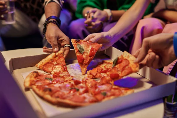 正方形の段ボール箱で食欲をそそるピザのスライスの閉じると若い友人の手がそれらを取って ホームパーティーを楽しみながら食べる — ストック写真
