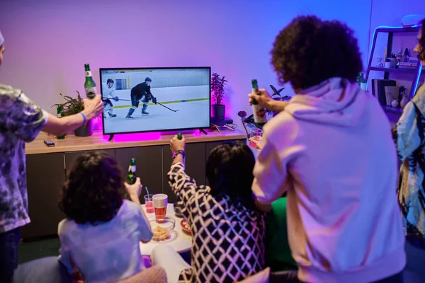 一群拿着啤酒的年轻朋友聚集在电视机前庆祝他们最喜爱的冰球队在主场的胜利 — 图库照片