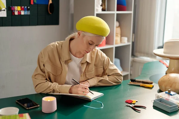 年轻而富有创造力的女人 一边用铅笔在笔记本上画新模特的草图 一边为新的季节性时装系列工作 — 图库照片
