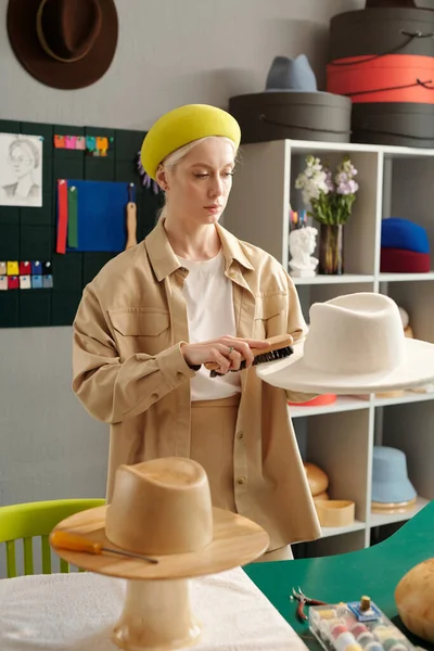 年轻的有创意的手工艺者和小手工艺店店主 在为顾客准备新衣服时 用刷子清洗白色毛毡帽 — 图库照片