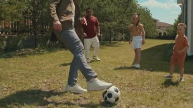 İki genç adam ve iki çocuk bahçede birlikte vakit geçiriyorlar. Birbirlerine top atıyorlar.