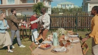 Genç siyah adam ve kız arkadaşı arkadaşlarını karşılıyor. Arka bahçede yaz için BBQ partisine davetliler.