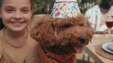 Partide doğum günü şapkası takan sevimli köpeğini okşayan neşeli ergen kızın seçici odak noktası.