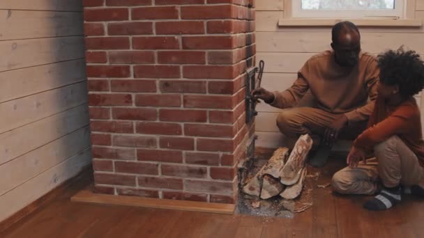 年轻的黑人解释他的儿子怎样给乡下的房子取暖 他的儿子把柴火加到柴堆里 — 图库视频影像