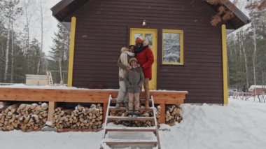 Kışlık giyimli modern Afro-Amerikan aile portresi. Karlı kış gününde, orman köyündeki kır evinin karşısında duruyor.