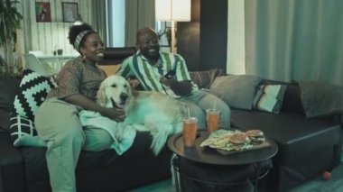 Oturma odasında kanepede oturan, akşamları televizyon izleyen Afrikalı Amerikalı genç kadın ve adamın solunda.