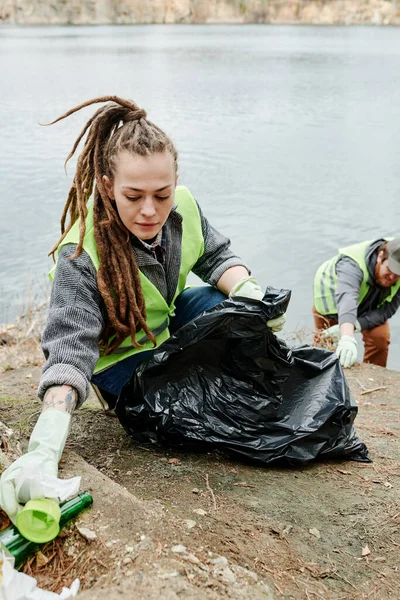 Młoda Kobieta Dredami Zbierająca Śmieci Jeziorze Wielkiej Czarnej Plastikowej Torbie — Zdjęcie stockowe